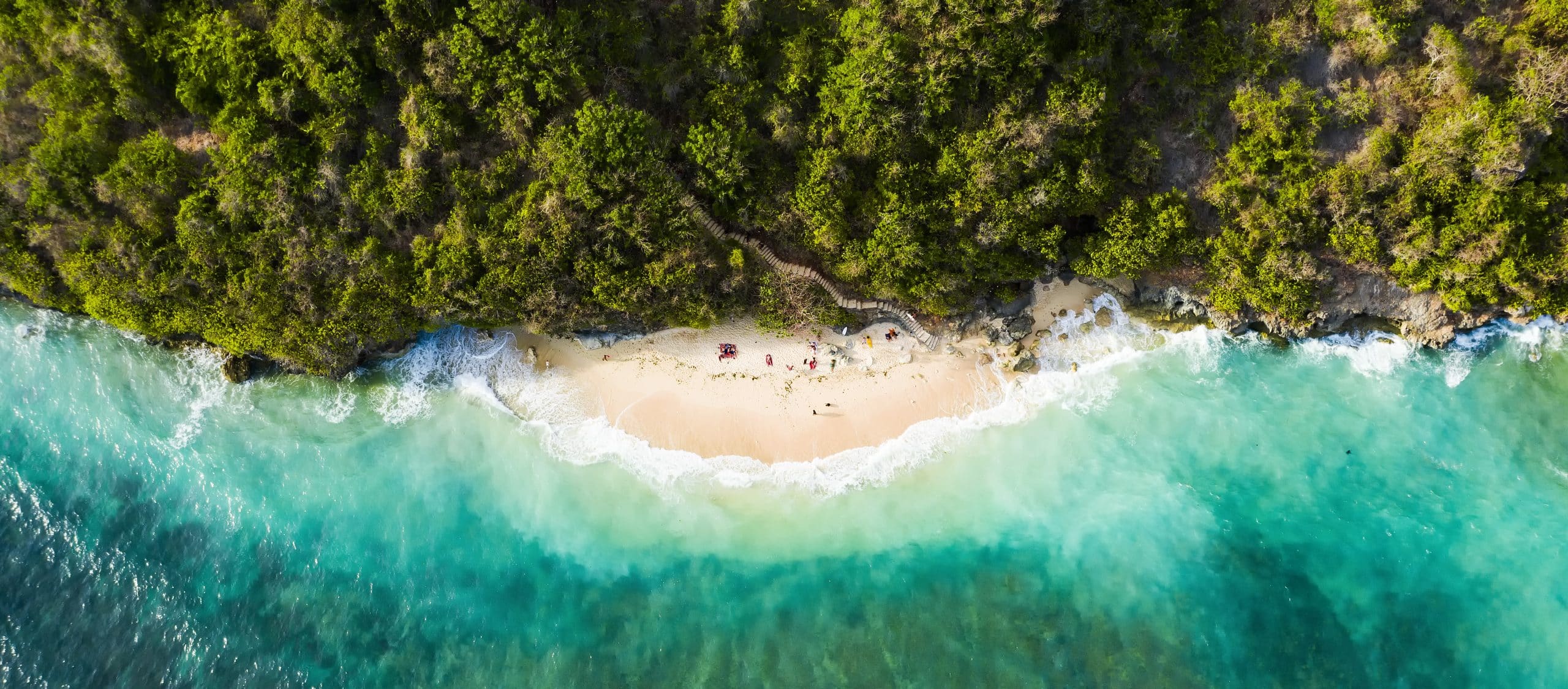 View from above, stunning aerial view of some tourists sunbathing on a beautiful beach bathed by a turquoise rough sea during sunset, Topan Beach, South Bali, Indonesia.