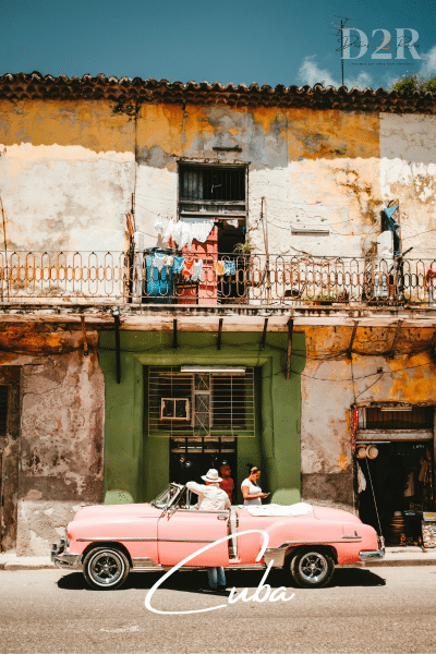 Photo d'une voiture de collection rose devant une vielle batisse à Cuba