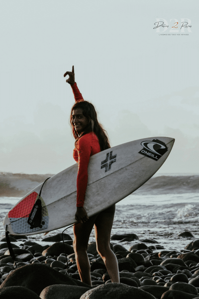 Surfeuse qui marche sur des cailloux pour aller surfer sur la plage de Tamanique au Salvador